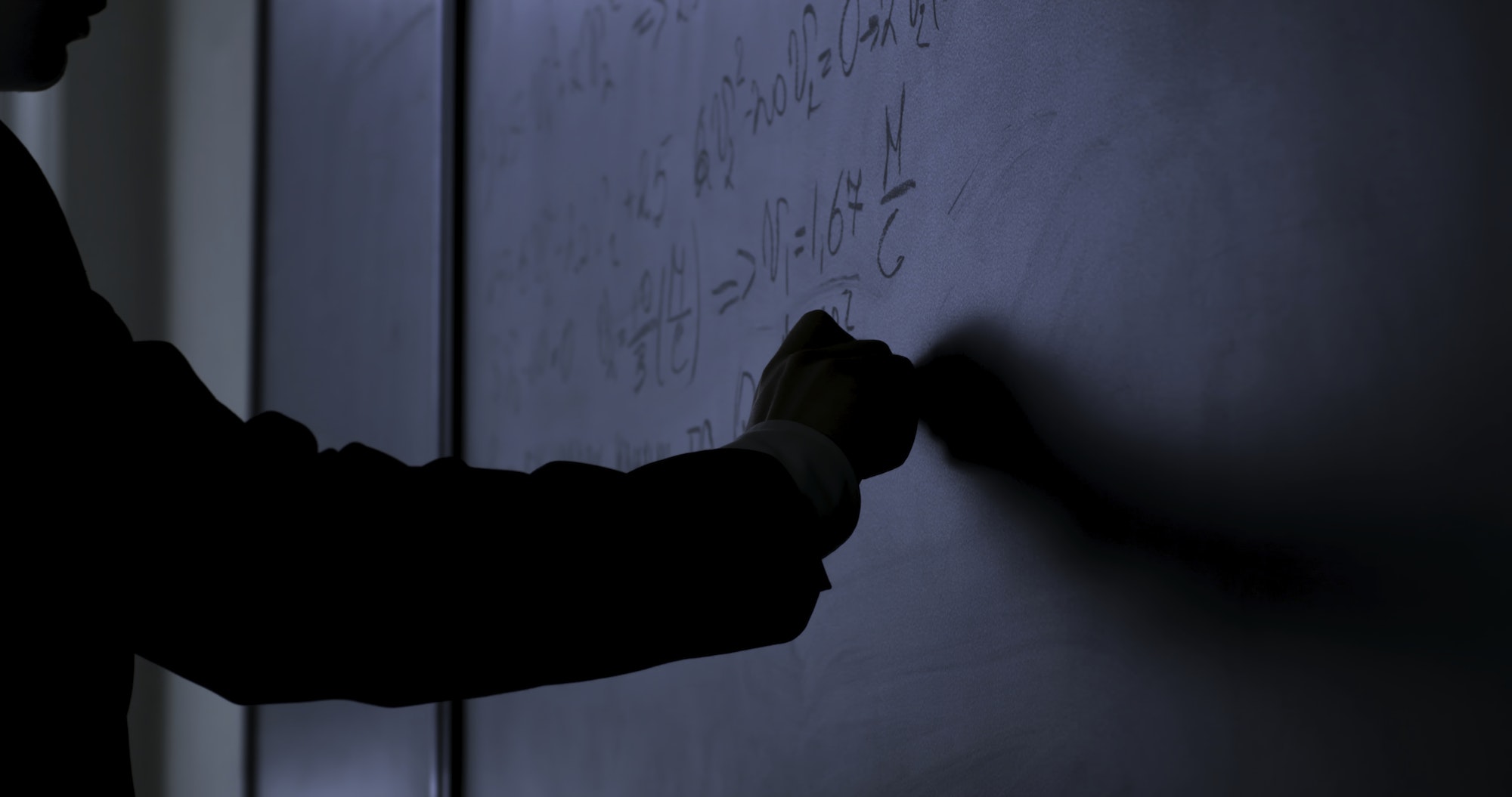 A person writing on a blackboard, explaining information