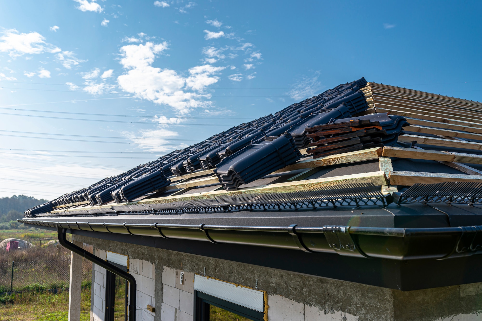 A roof in the middle of construction, with roof tiles and beams visible against a clear sky