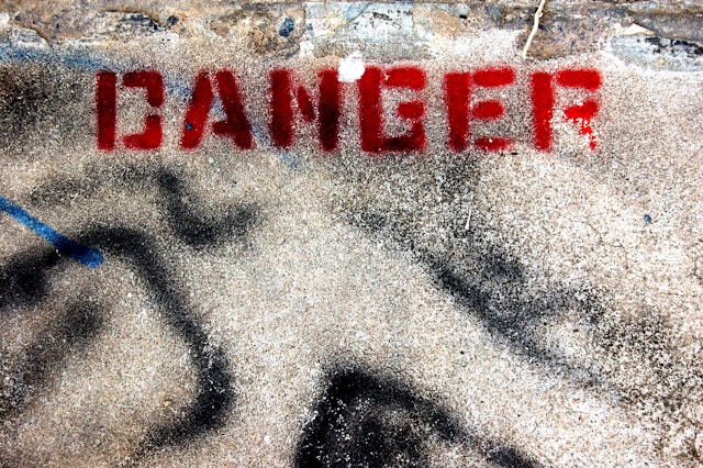 A close-up of graffiti on a concrete wall with the word 'DANGER' spray-painted in red.